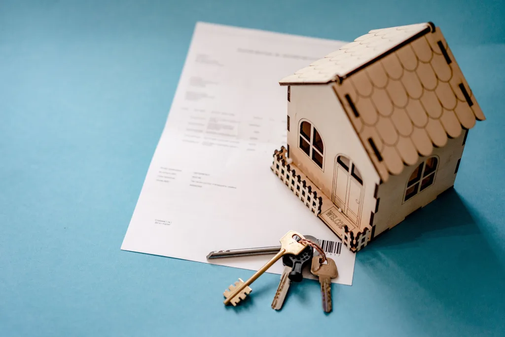 A wooden house and some keys are on top of a mortgage contract.