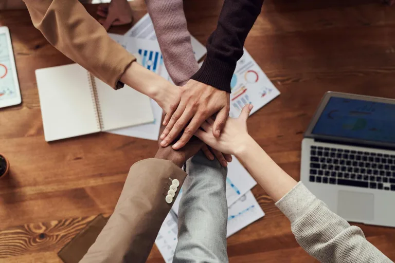 A diverse team of business people joining hands over a table, illustrating partnership and shared commitment to success.