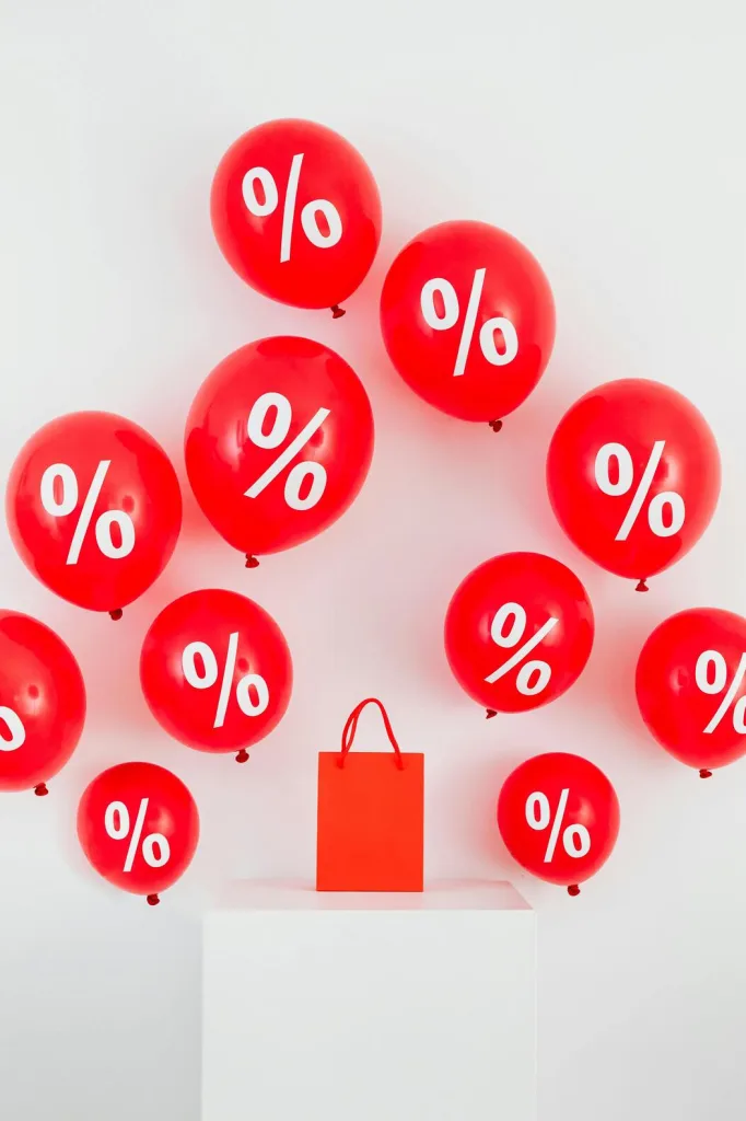 Red balloons featuring a percent sign alongside a shopping bag, symbolizing discounts and shopping promotions.