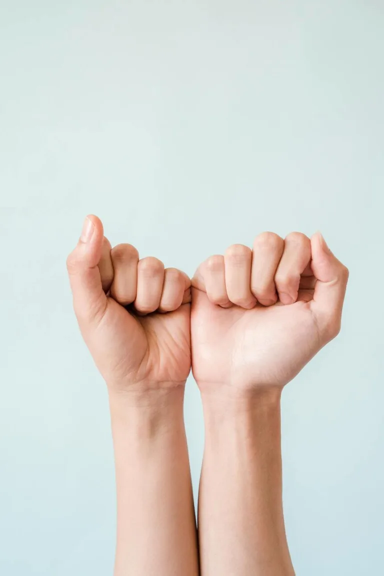 Two hands with clenched fists raised against a vibrant blue background, symbolizing strength and unity.