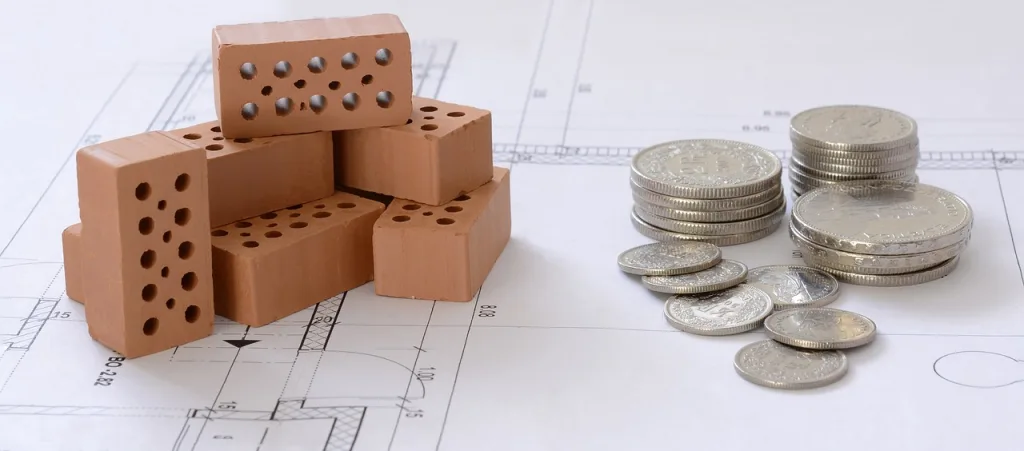 A stack of bricks and coins rests atop a detailed blueprint, symbolizing construction and financial planning.