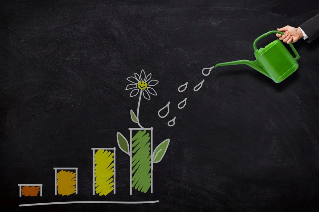 A businessman waters a flower on a chalkboard, symbolizing growth with a chart in the background.