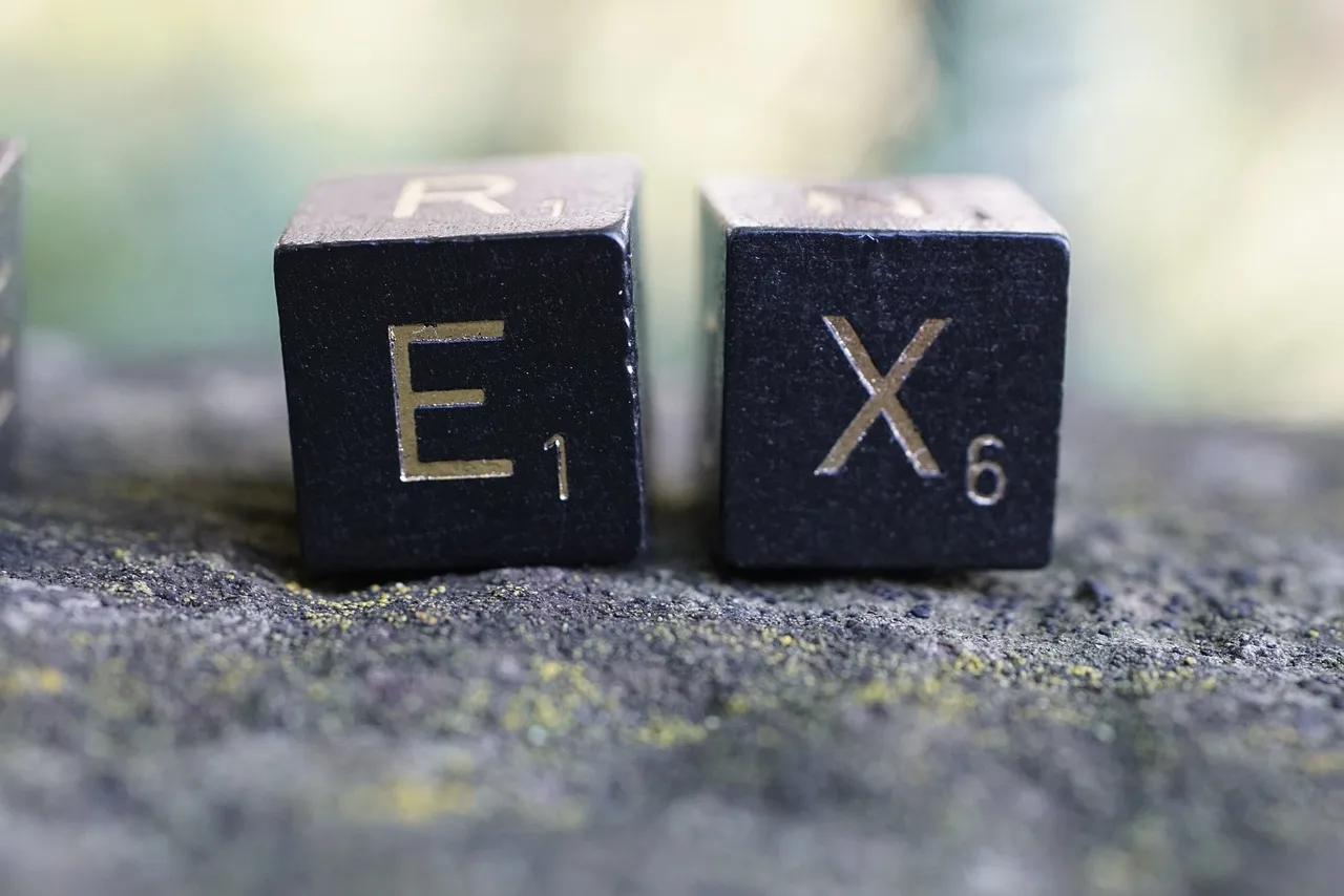 Two black Scrabble tiles on a textured surface, each displaying a letter: E with a point value of 1, and X with a point value of 6. In the background, there is a subtle, blurred mix of green and yellow hues.