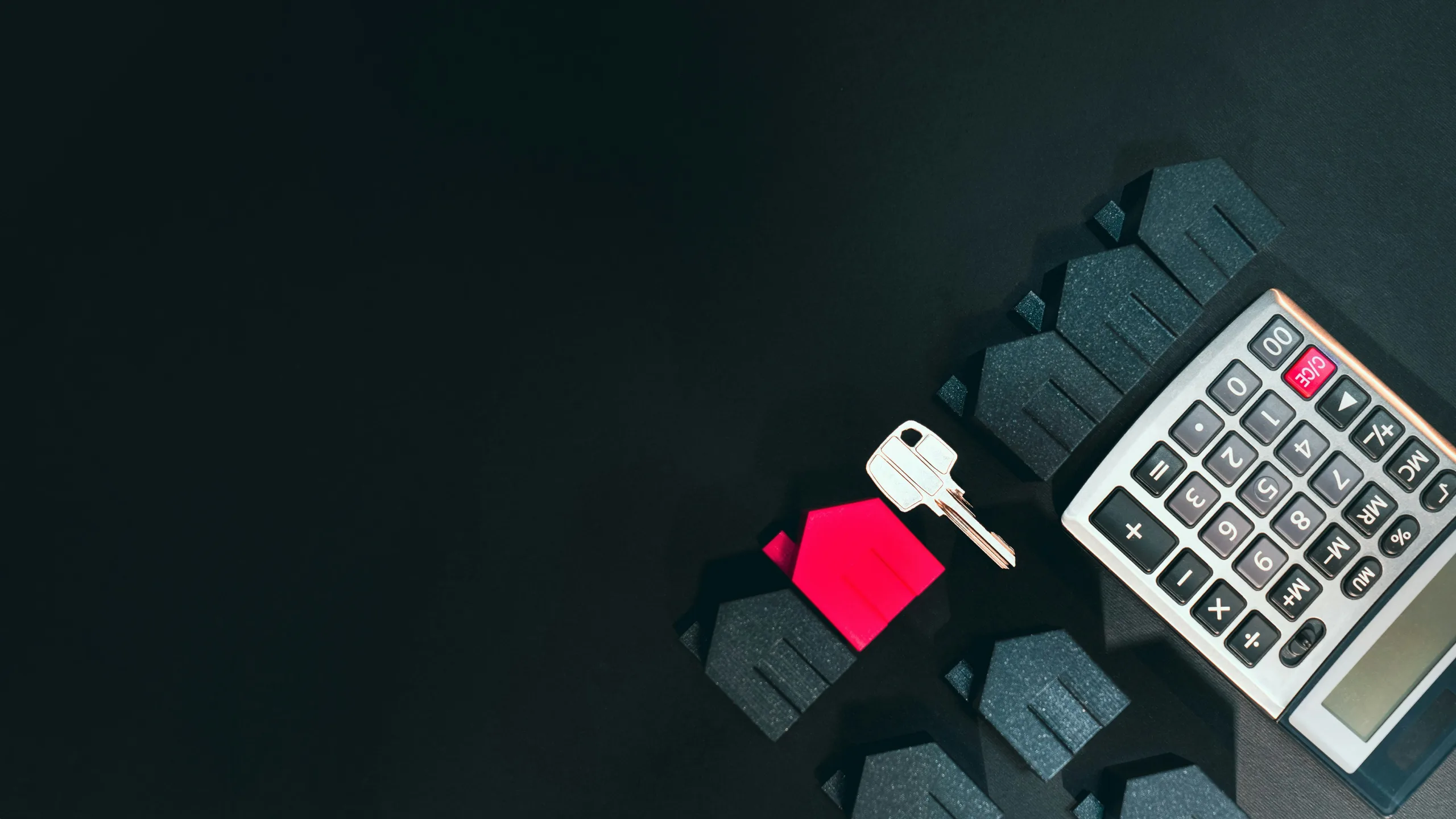 A calculator and keys placed beside a house model on a sleek black surface, symbolizing financial planning for homeownership.